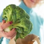 Mulher retirando um vegetal da sacola do supermercado.
