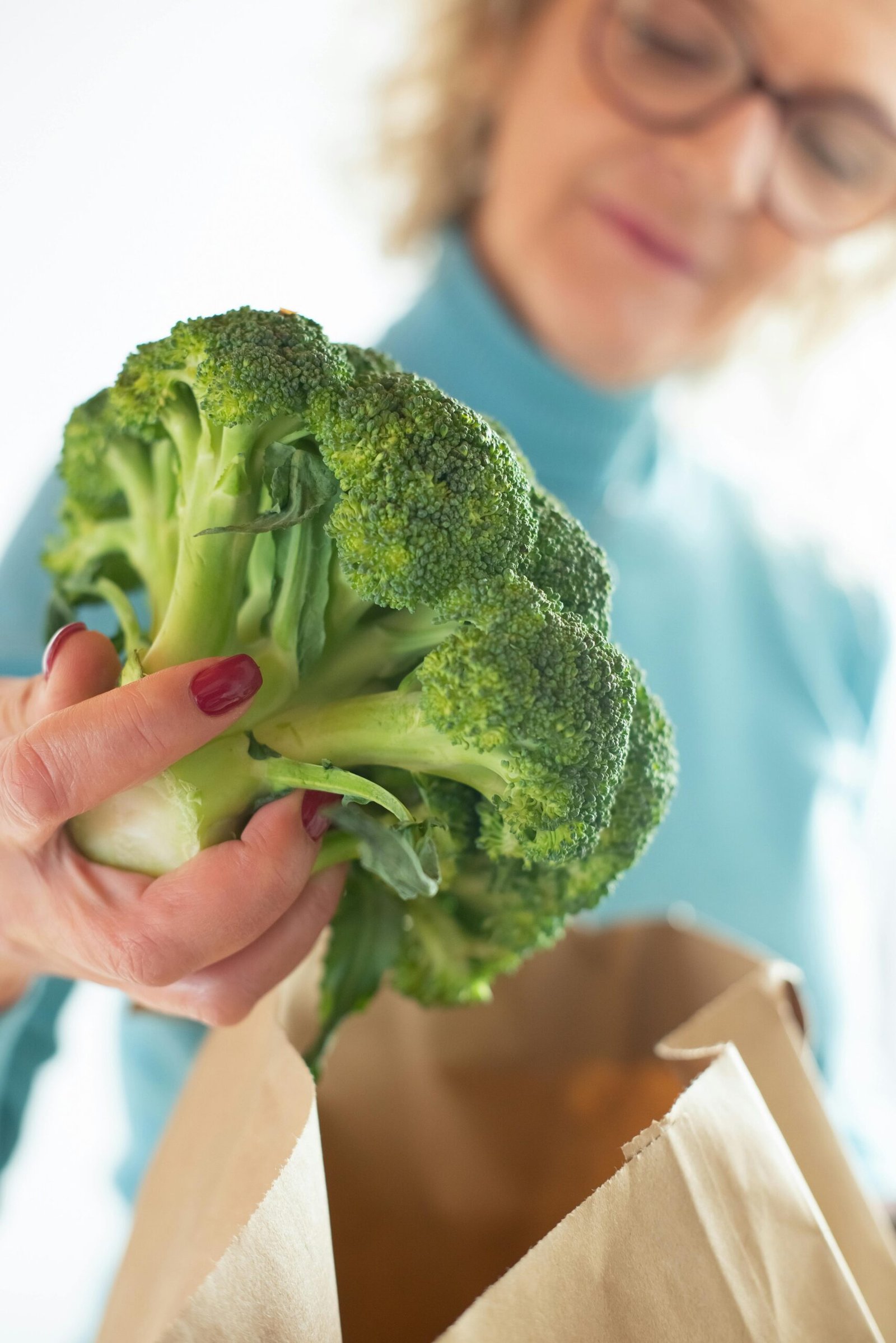 Mulher retirando um vegetal da sacola do supermercado.